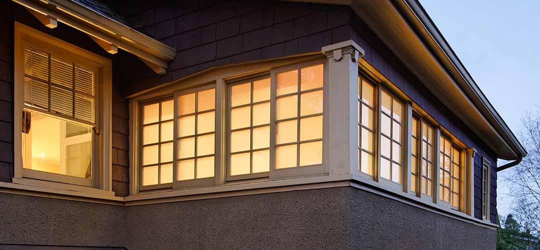 A close up on a residential house's windows with a soft yellow light shining through them.